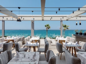 An outdoor dining area with tables and chairs, overlooking the ocean. - Ikones Seafront Luxury Suites (Rethymno)