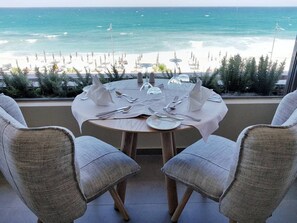 A round table with a white tablecloth, two grey upholstered chairs, and a view of the ocean and beach. - Ikones Seafront Luxury Suites (Rethymno)
