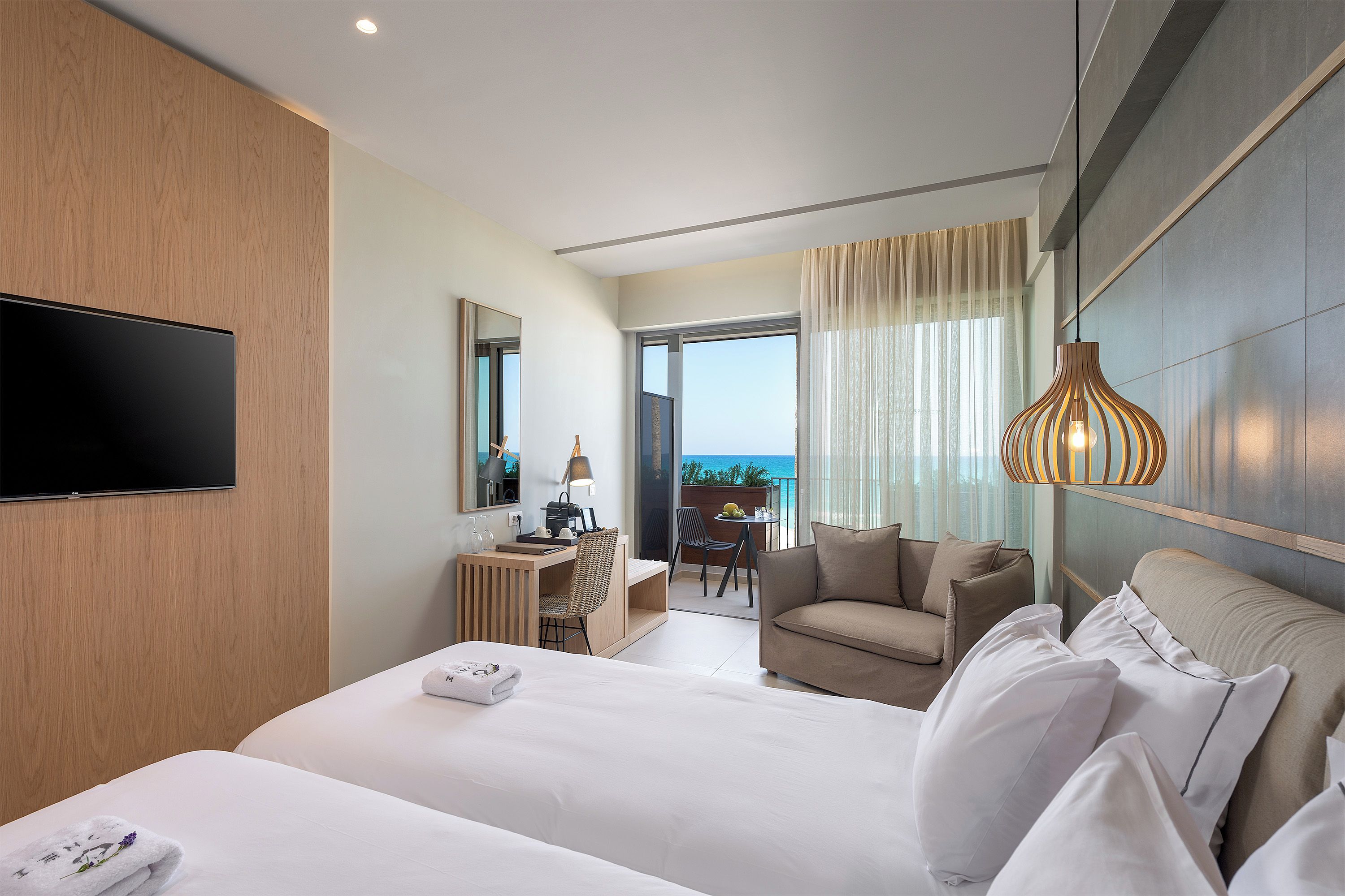 A hotel room with a large bed, a desk, a chair, a sofa, a TV, and a balcony with a view.