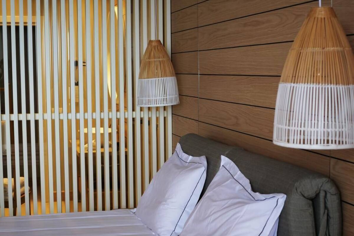 Een bed met witte lakens en twee kussens, een houten wand en twee hangende rieten lampen.