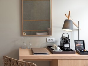 A modern workspace with a desk, a lamp, a coffee machine, and a tray with cups and a notebook. - Ikones Seafront Luxury Suites (Rethymno)