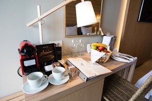 Dans une chambre d’hôtel, on trouve un buffet de petit-déjeuner avec une machine à café, un panier de fruits, un menu et une lampe.