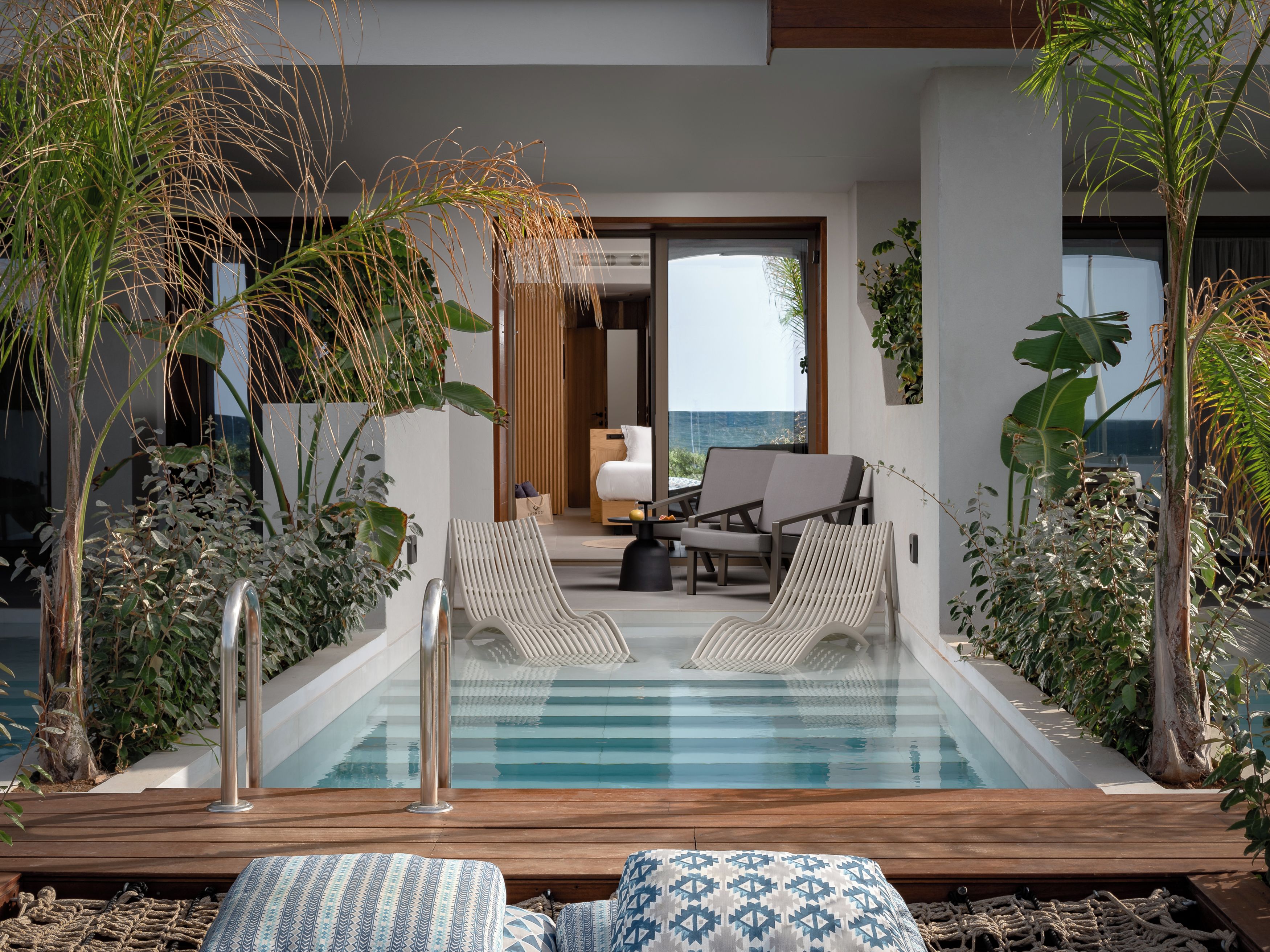 A pool area with lounge chairs, a wooden deck, and a view of the ocean.