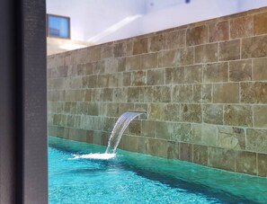 A swimming pool with a waterfall feature against a stone wall. - Ikones Seafront Luxury Suites (Rethymno)