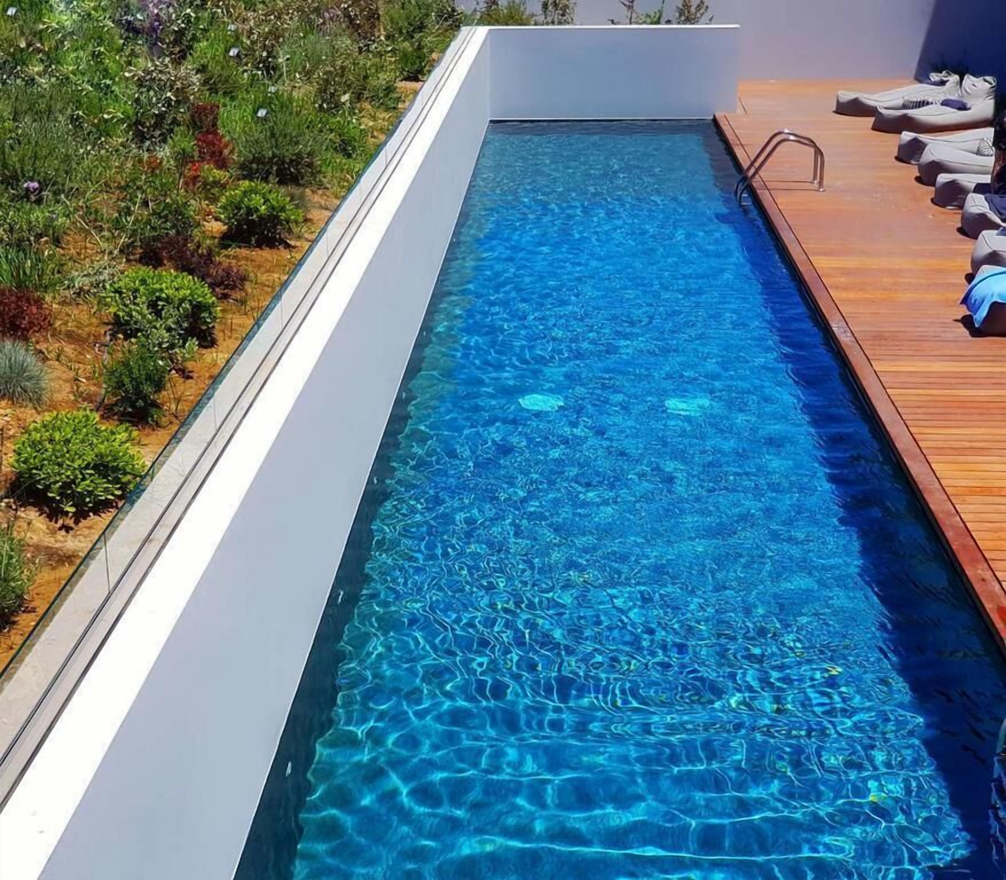 Una piscina moderna con agua cristalina azul, rodeada por un muelle de madera y diversas plantas.