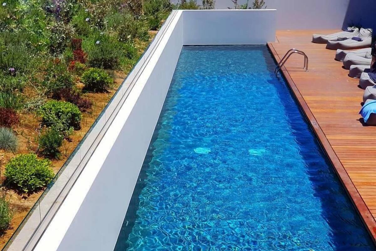 Een zwembad in moderne stijl met helderblauw water, omringd door een houten terras en diverse planten.