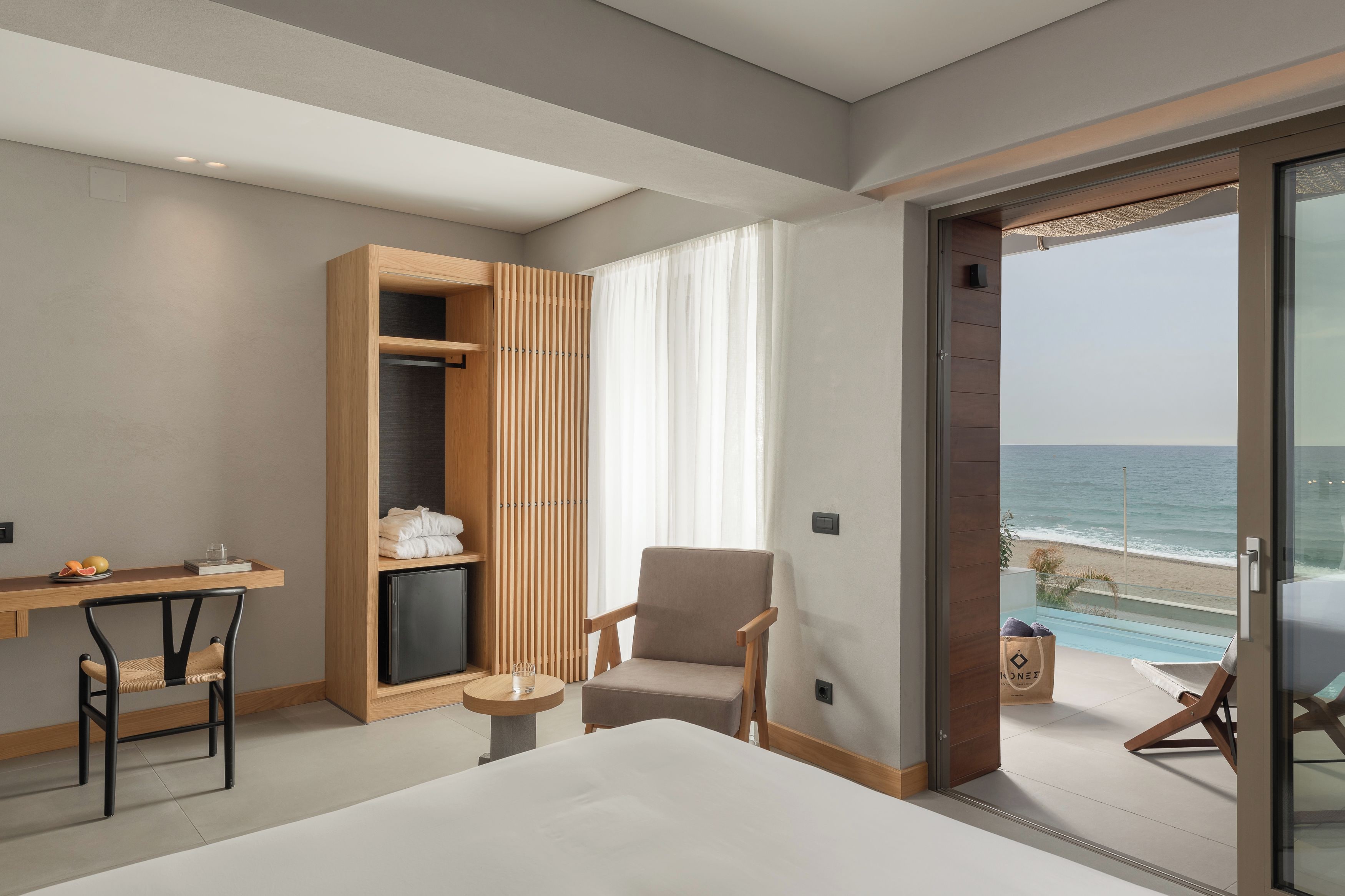 Ein modernes Hotelzimmer mit Bett, Schreibtisch, Stuhl, Fernseher und Blick auf den Strand.