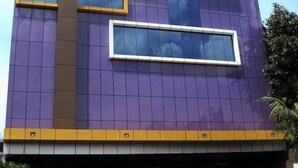 A multi-story building with a purple facade, large windows, and a yellow trim. - Alma Hotel (Jakarta)