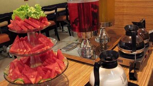 A buffet setup with watermelon slices, a salad, and a beverage station with two pitchers. - Alma Hotel (Jakarta)