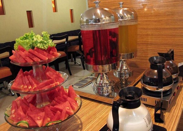 A buffet setup with watermelon slices, a salad, and a beverage station with two pitchers. - Alma Hotel (Jakarta)