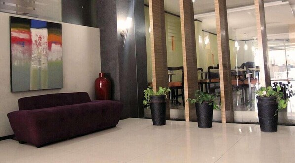 Un área de recepción con un sofá púrpura, un jarrón rojo y plantas en macetas.