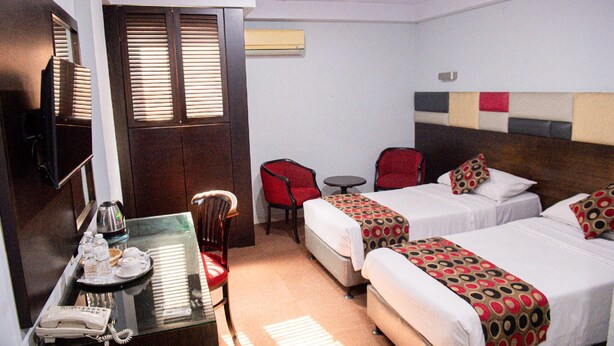 A hotel room with two beds, a desk with a telephone, a chair, a small table, and an air conditioning unit. - Alma Hotel (Jakarta)