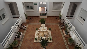 A courtyard with a central fountain, surrounded by potted plants and white railings. - Aparthotel Vistamar (Nijar)