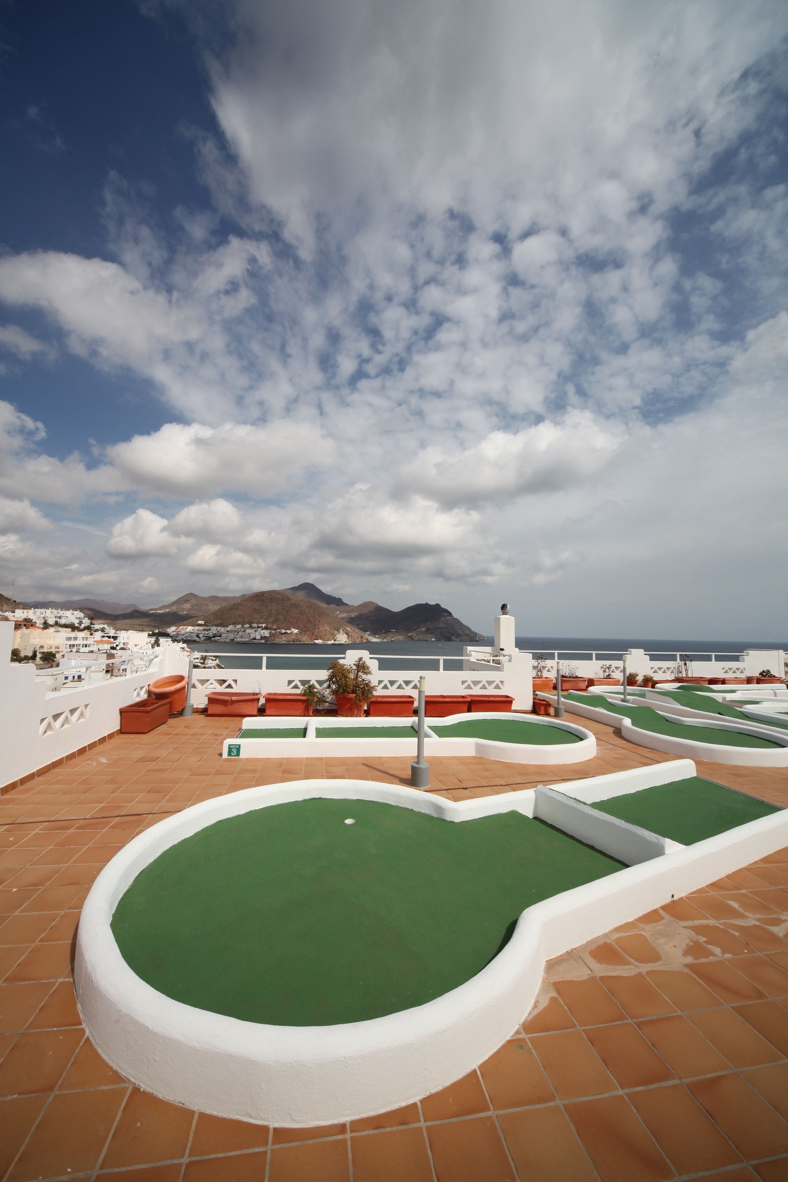 A rooftop with green artificial grass, white walls, and a view of the sea and mountains.
