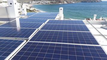 Paneles solares en un tejado con un pueblo costero y montañas al fondo.