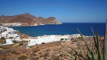 Un pueblo costero con edificios blancos, un mar azul cristalino y montañas al fondo.