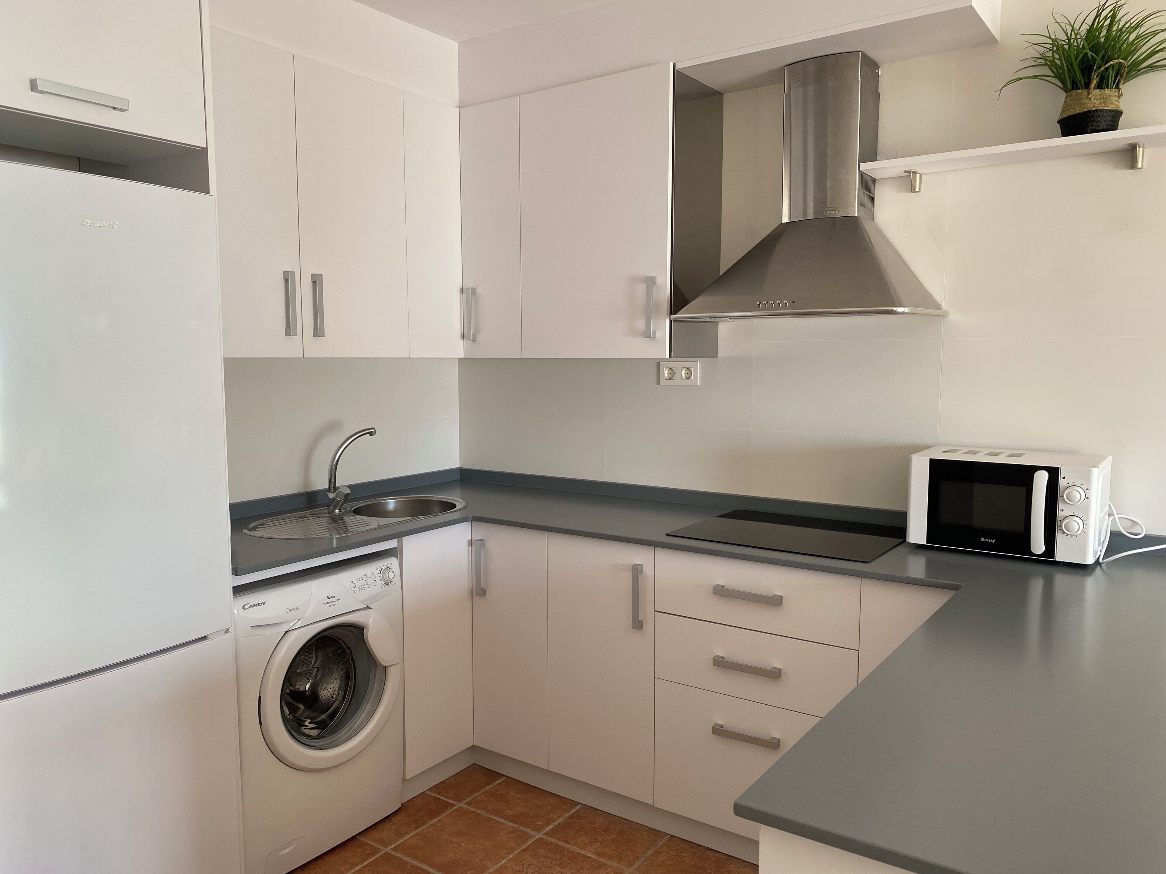 Une cuisine moderne avec des meubles blancs, un évier en acier inoxydable, un four à micro-ondes et un lave-linge.