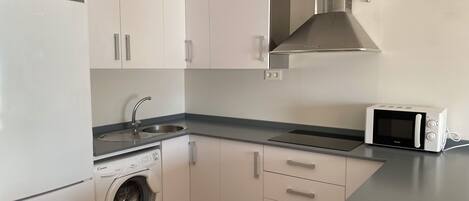 Une cuisine moderne avec des meubles blancs, un évier en acier inoxydable, un four à micro-ondes et un lave-linge.