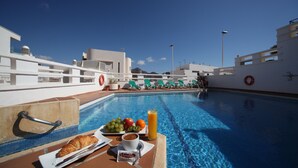 A poolside breakfast setup with croissants, coffee, fruit, and juice. - Aparthotel Vistamar (Nijar)