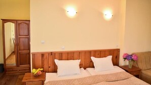 A bedroom with a wooden headboard, two bedside lamps, a nightstand with a fruit bowl, and a vase with flowers. - Lina Guest House (Bansko)