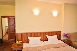 Quarto com cabeceira de madeira, duas luminárias de cabeceira, mesa de cabeceira com uma tigela de frutas e um vaso com flores.