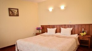 A neatly made bed with a wooden headboard, a nightstand with a vase of flowers, and a wall-mounted picture. - Lina Guest House (Bansko)