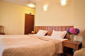 A hotel room with a double bed, two bedside tables, a wooden headboard, and a nightstand with a vase of flowers.