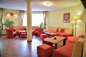 A hotel room with a sofa, chairs, a table, and a lamp.