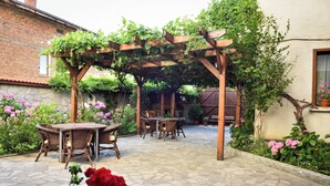 A patio with stone flooring, wooden pergola, wicker furniture, and potted plants. - Lina Guest House (Bansko)