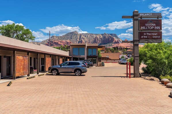 A hotel with a signboard indicating a vacancy, a parking area, and a mountainous backdrop. - Sedona Hilltop Inn (Sedona)