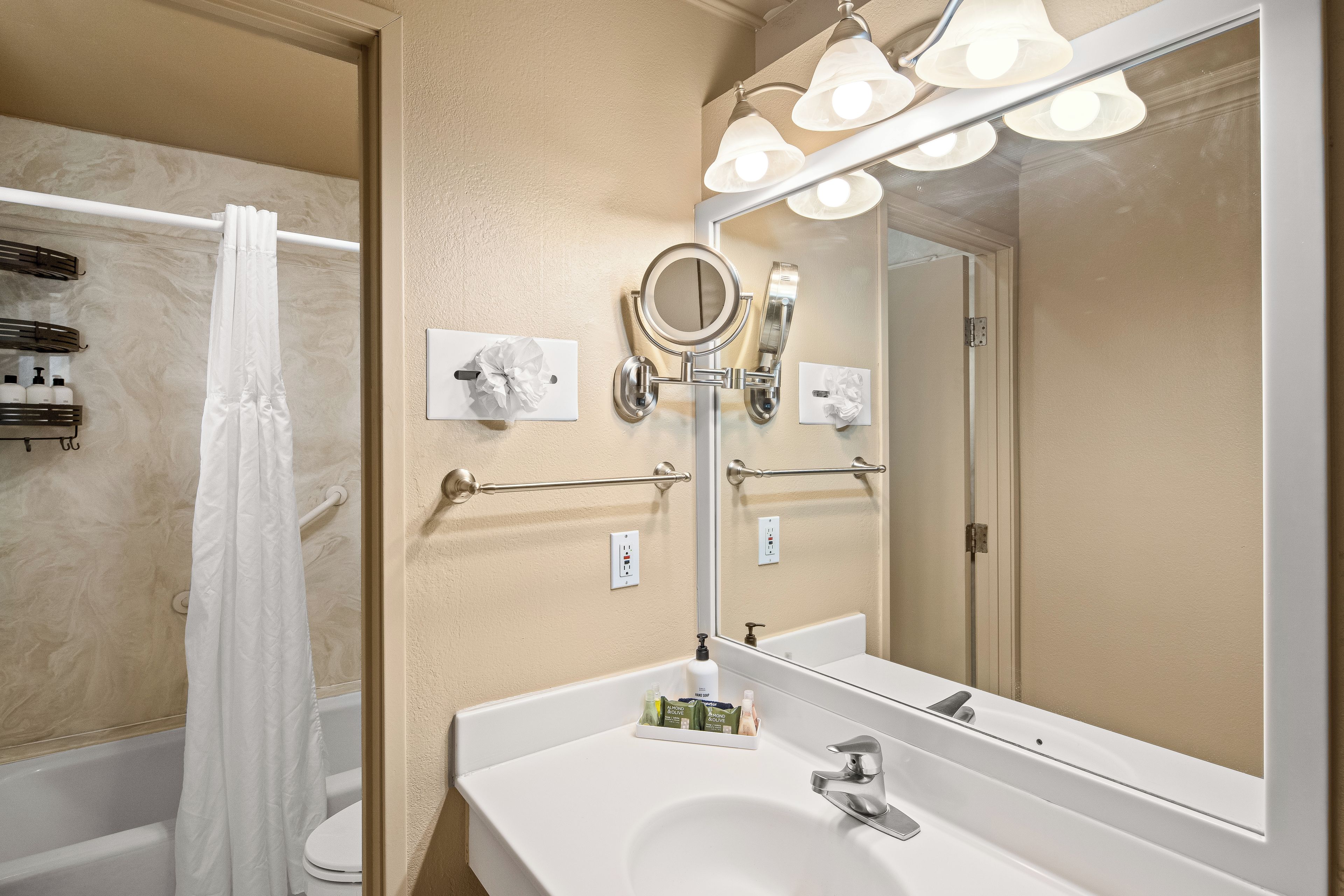 A bathroom with a white sink, a mirror with lights, a towel rack, and a shower curtain.