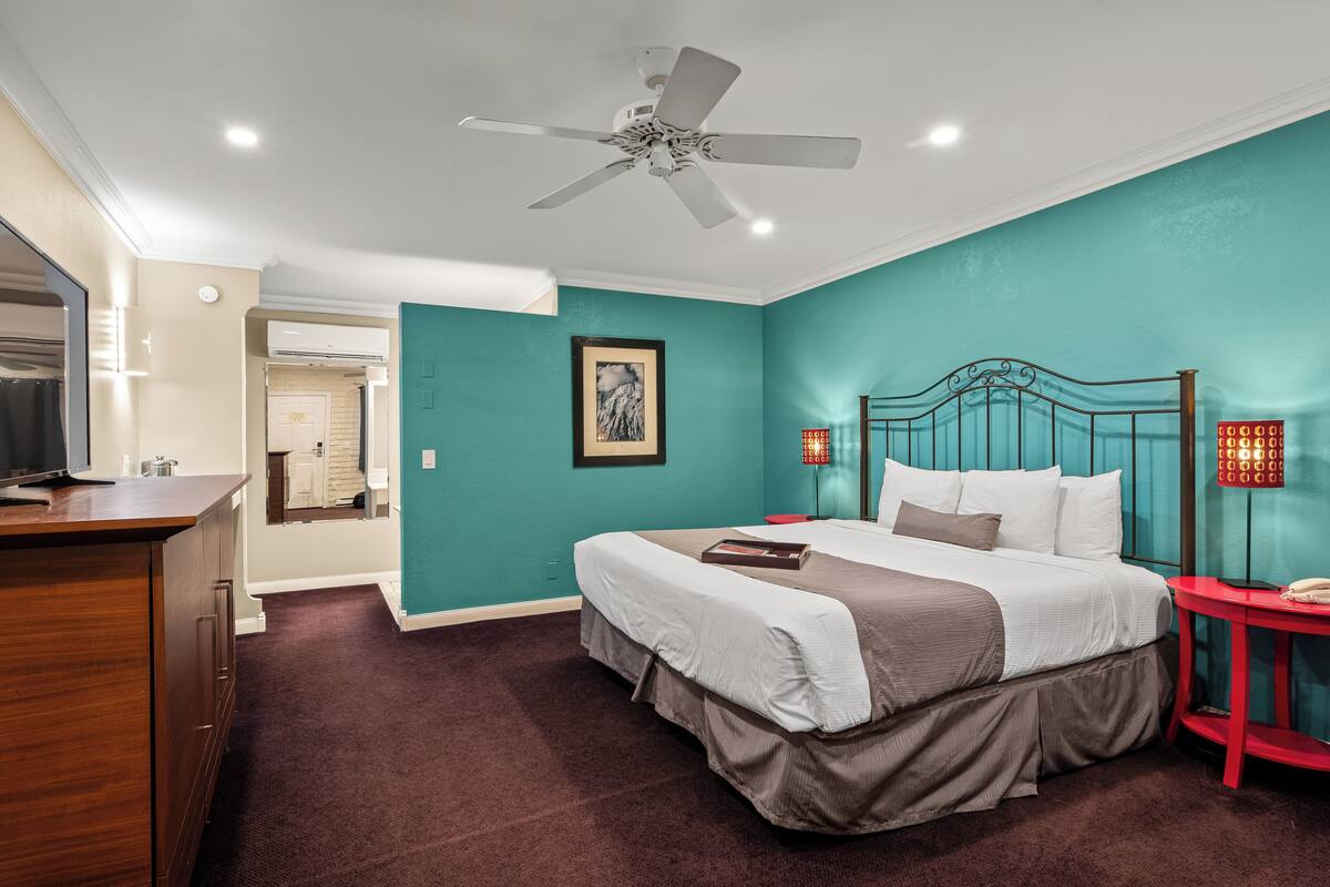 A bedroom with a bed, a desk, a ceiling fan, and a red side table.