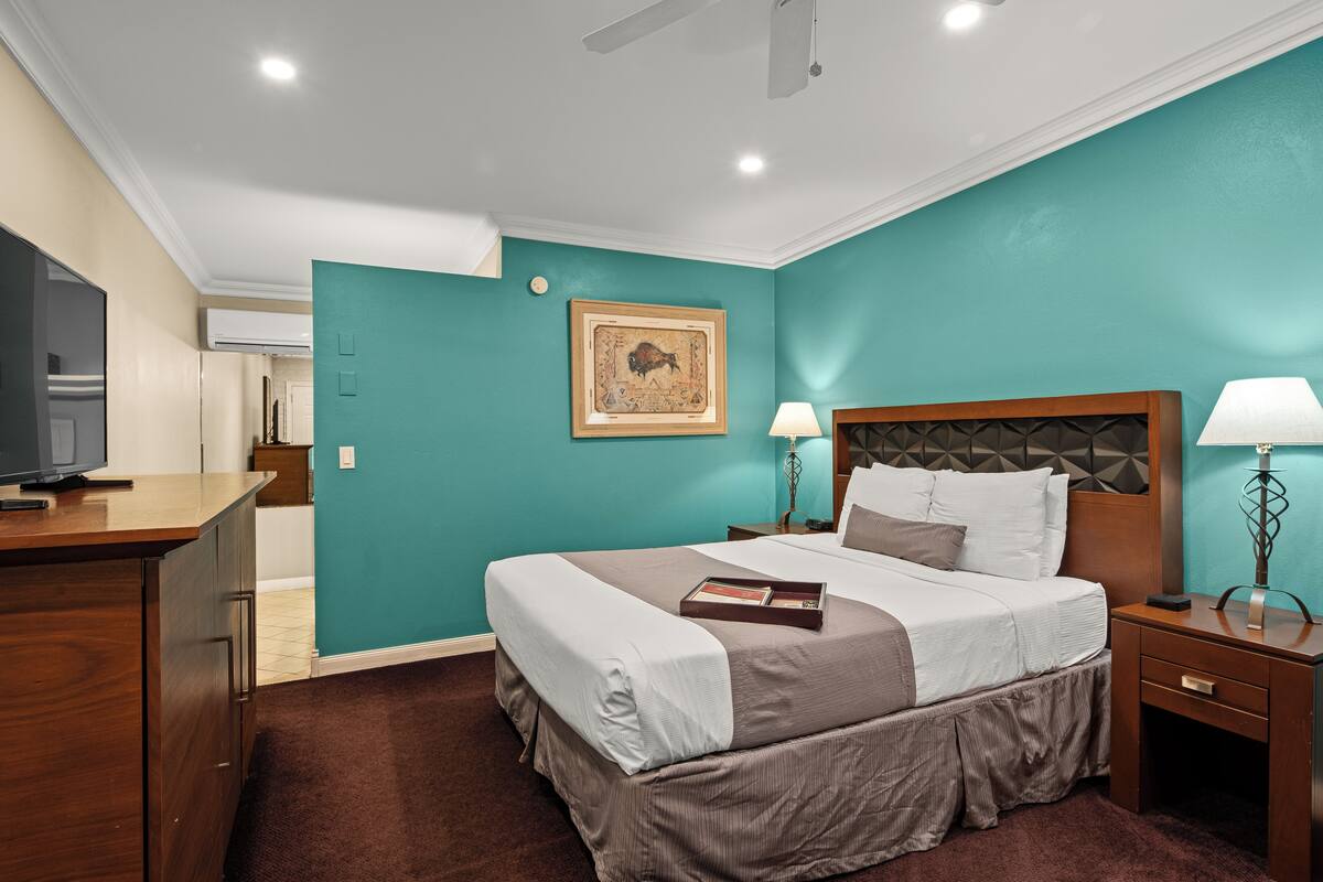 A hotel room with a bed, bedside tables, a TV, and a painting on the wall.