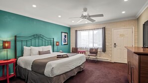 A hotel room with a bed, a desk, a chair, a ceiling fan, and a window.