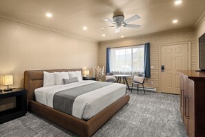 A hotel room with a bed, bedside tables, a desk, a chair, a window with curtains, a door, and a ceiling fan. - Sedona Hilltop Inn (Sedona)