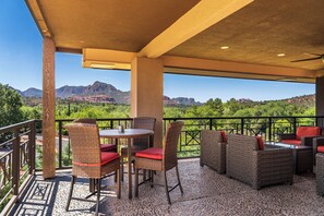 A covered outdoor seating area with wicker furniture and red cushions, overlooking a mountainous landscape. - Sedona Hilltop Inn (Sedona)