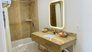 A bathroom with a bathtub, a sink with a granite countertop, a mirror with a light, and a towel rack. - Escondido Inn (Escondido)