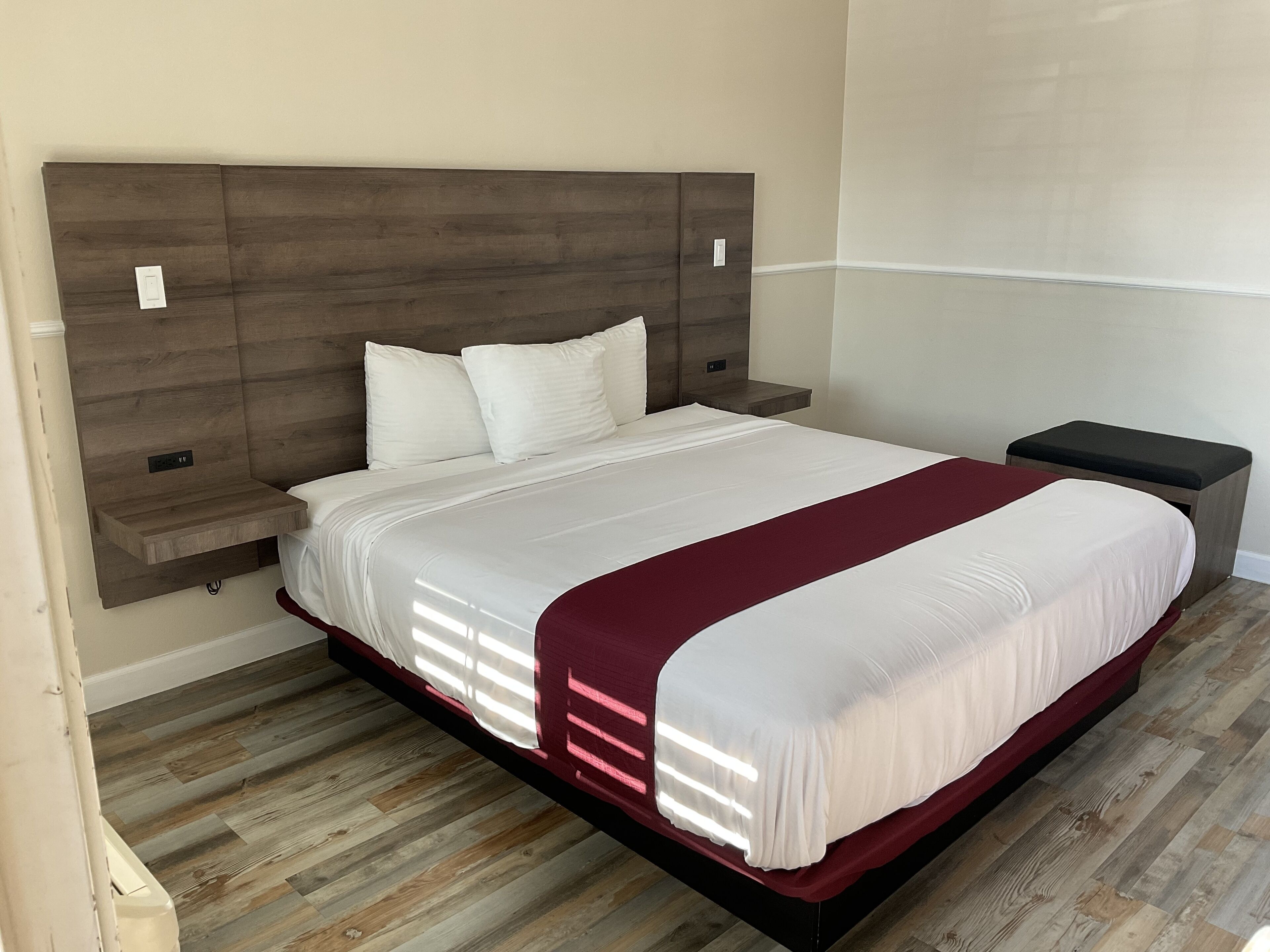 Cama bem arrumada com cabeceira de madeira, roupa de cama branca e detalhe em vermelho.