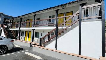 Een motel met meerdere verdiepingen, een centrale trap, een geparkeerde auto ervoor en een heldere blauwe lucht.