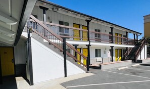 A multi-story hotel with a white facade, yellow doors, and a central staircase with brown railings.