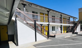 Un hotel de varios pisos con fachada blanca, puertas amarillas y una escalera central con barandales marrones.