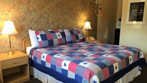 A neatly made bed with a star-patterned quilt, two bedside lamps, a wooden nightstand, and a floral wallpaper background. - Sharon Motel (Wells)