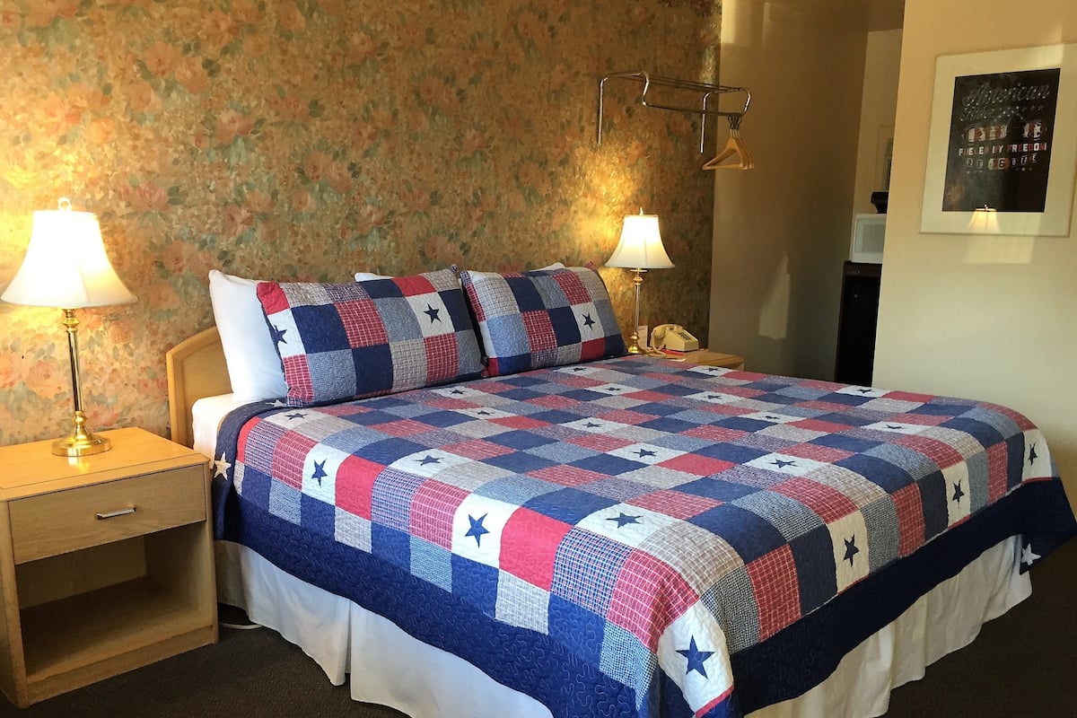 A neatly made bed with a star-patterned quilt, two bedside lamps, a wooden nightstand, and a floral wallpaper background.