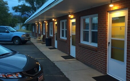 A motel with a row of rooms, each with a door and a window. There is a car parked in front.