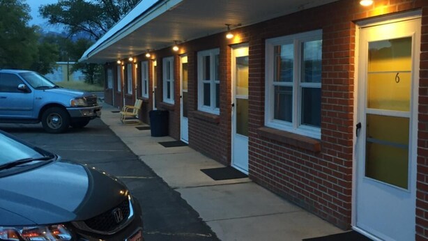 A motel with a row of rooms, each with a door and a window. There is a car parked in front. - Sharon Motel (Wells)