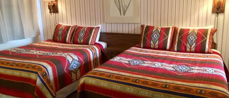 Une chambre double avec deux lits, chacun agrémenté de draps et d’oreillers à motifs. Des lampes murales sont fixées de chaque côté des lits.
