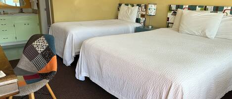 A hotel room with two beds, a desk, a chair, and a mirror.