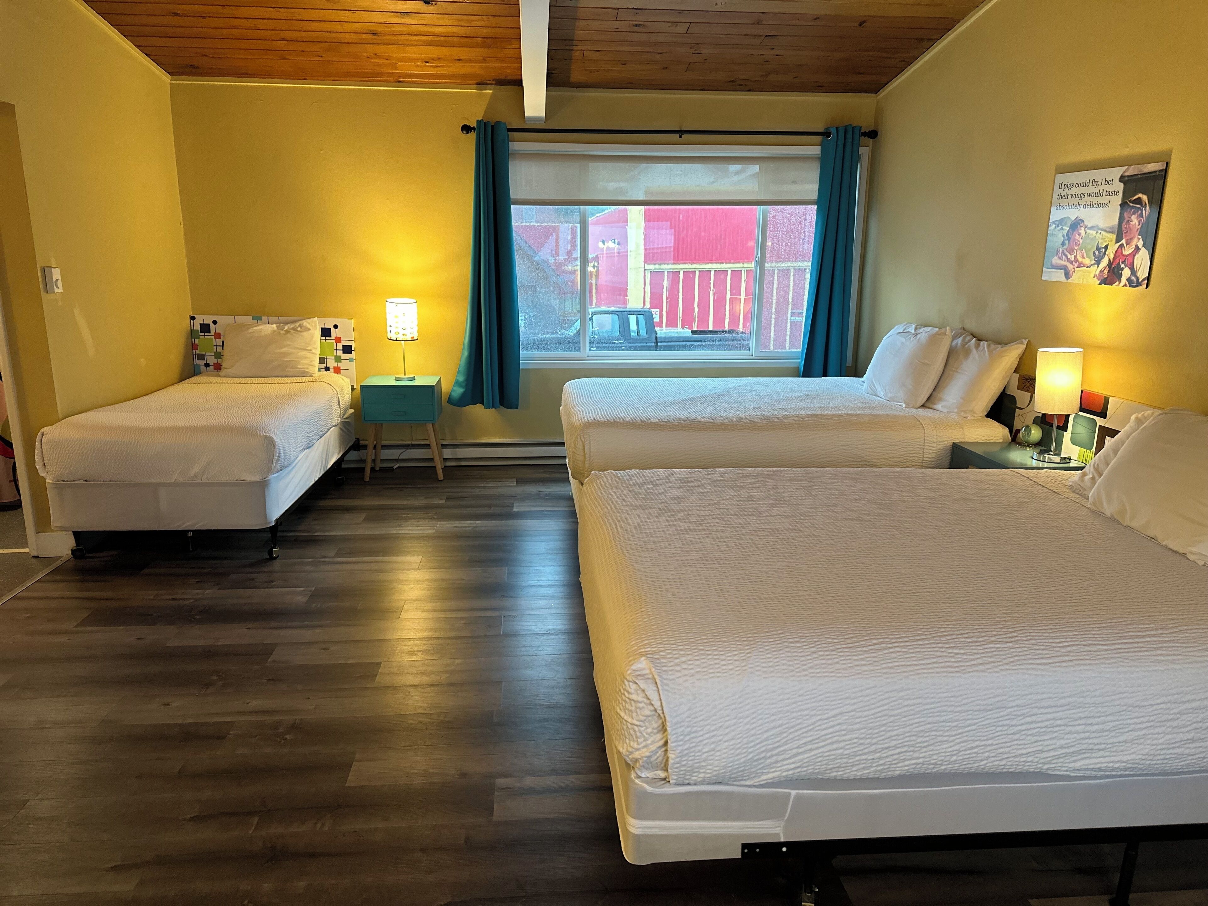 Habitación de hotel con dos camas individuales, una mesita con lámpara, una ventana con cortinas y un cartel en la pared.