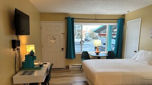A hotel room with a bed, a desk with a chair, a television, and a window with curtains.