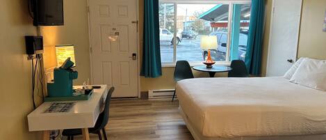 A hotel room with a bed, a desk with a chair, a television, and a window with curtains.